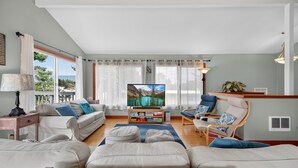 Un salon comprenant un canapé, des fauteuils, une table basse, un téléviseur et donnant sur l’extérieur.