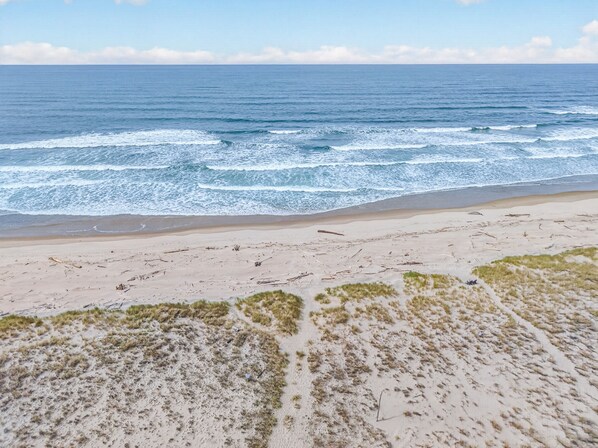 Ein Strand mit Wellen, Sand und spärlicher Vegetation.