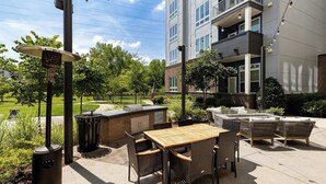 An outdoor patio with a grill, wicker furniture, and a view of a building. - Landing Apartments Charlotte - NoDA (Charlotte)