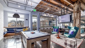 A modern lounge area with a pool table, seating, and a large TV screen. - Landing Apartments Charlotte - NoDA (Charlotte)