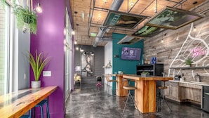 A modern bar area with a wooden counter, bar stools, and a television screen. - Landing Apartments Charlotte - NoDA (Charlotte)