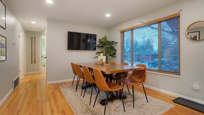 A dining area with a wooden table and chairs, a potted plant, and a large window with blinds. - Central Gem ~ Backyard Oasis with Hot Tub and Firepit (Arvada)