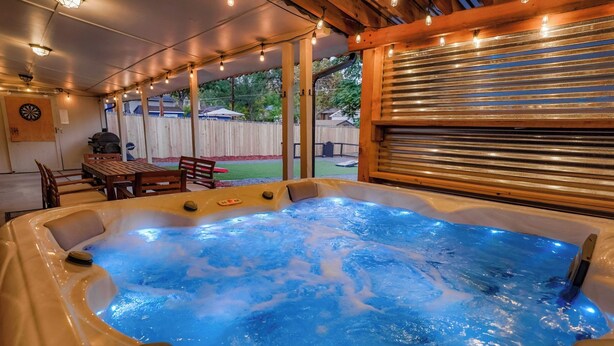 A hot tub with a wooden deck and string lights, surrounded by a wooden fence and a covered patio area. - Central Gem ~ Backyard Oasis with Hot Tub and Firepit (Arvada)