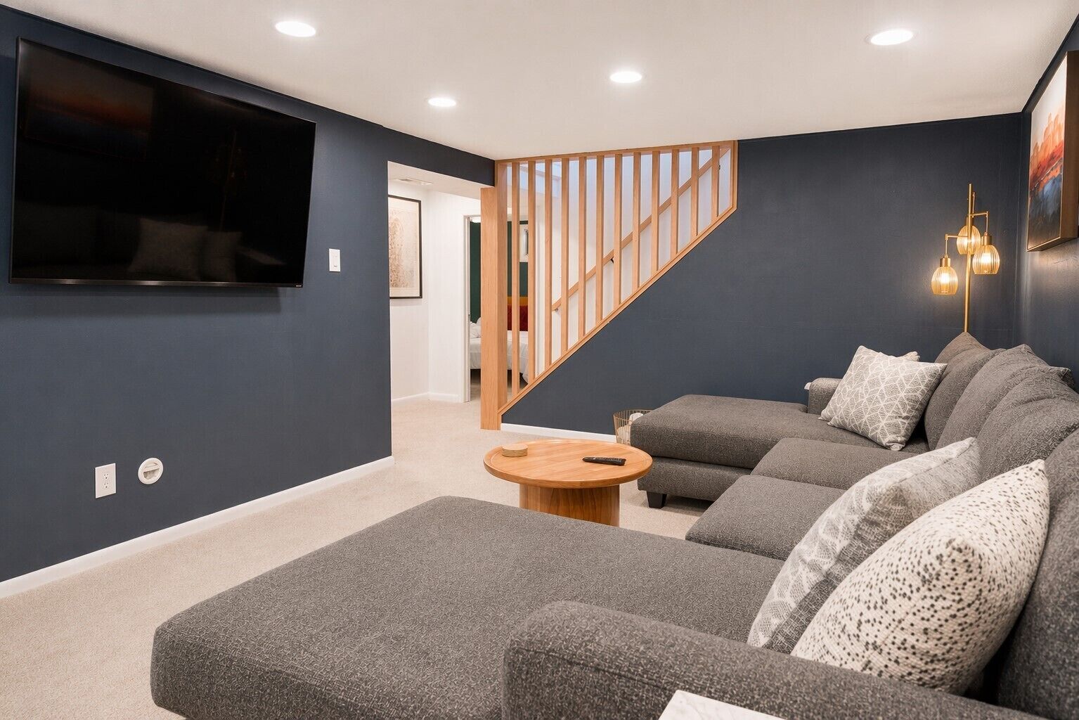A modern living room with a grey sectional sofa, a wooden coffee table, and a TV mounted on the wall.