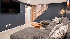 A modern living room with a grey sectional sofa, a wooden coffee table, and a TV mounted on the wall. - Central Gem ~ Backyard Oasis with Hot Tub and Firepit (Arvada)