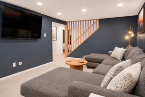 A modern living room with a grey sectional sofa, a wooden coffee table, and a TV mounted on the wall. - Central Gem ~ Backyard Oasis with Hot Tub and Firepit (Arvada)