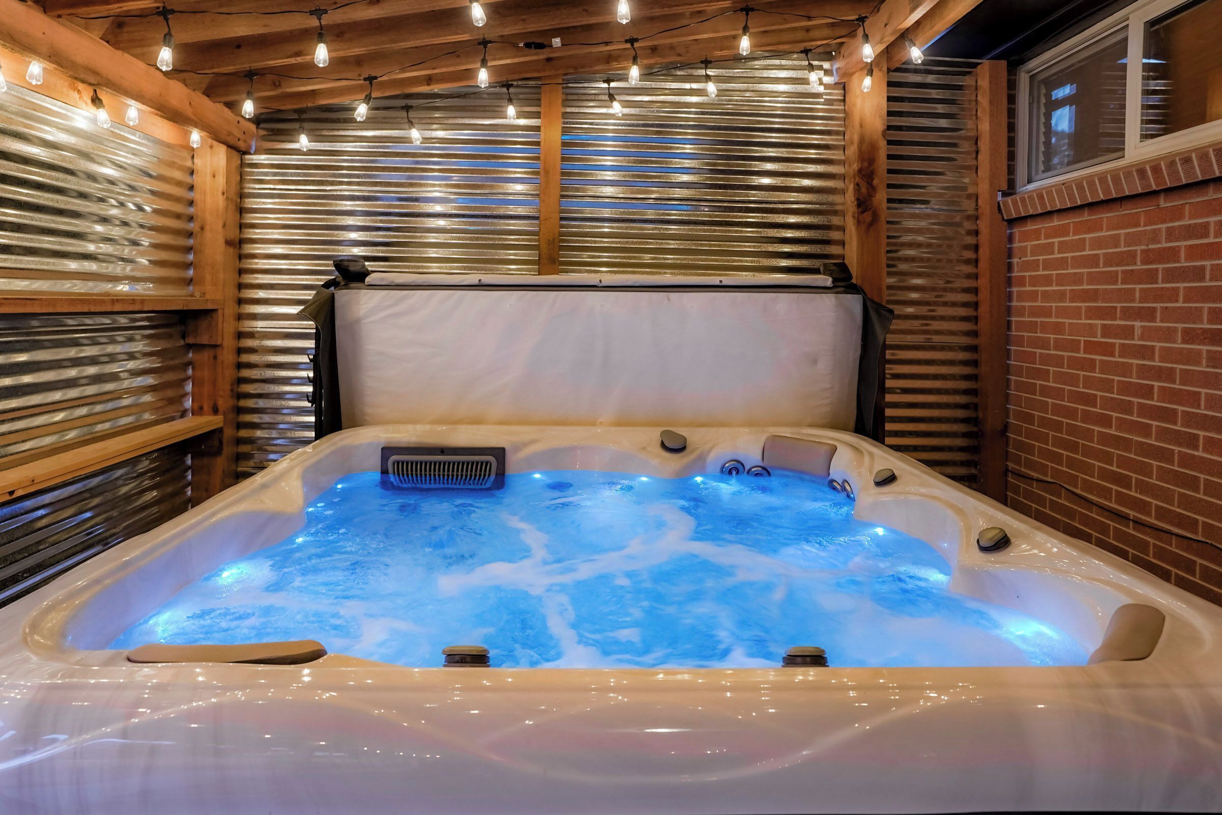 A hot tub with a wooden ceiling and metal walls, surrounded by string lights.