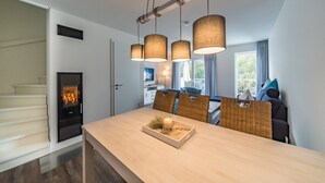 A modern dining area with a wooden table, hanging pendant lights, wicker chairs, and a fireplace.