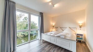 A bedroom with a large window, a bed, bedside lamps, and a nightstand.