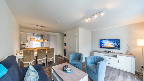 A modern living room with a sofa, armchairs, a coffee table, a TV, and a dining area with chairs and a table.