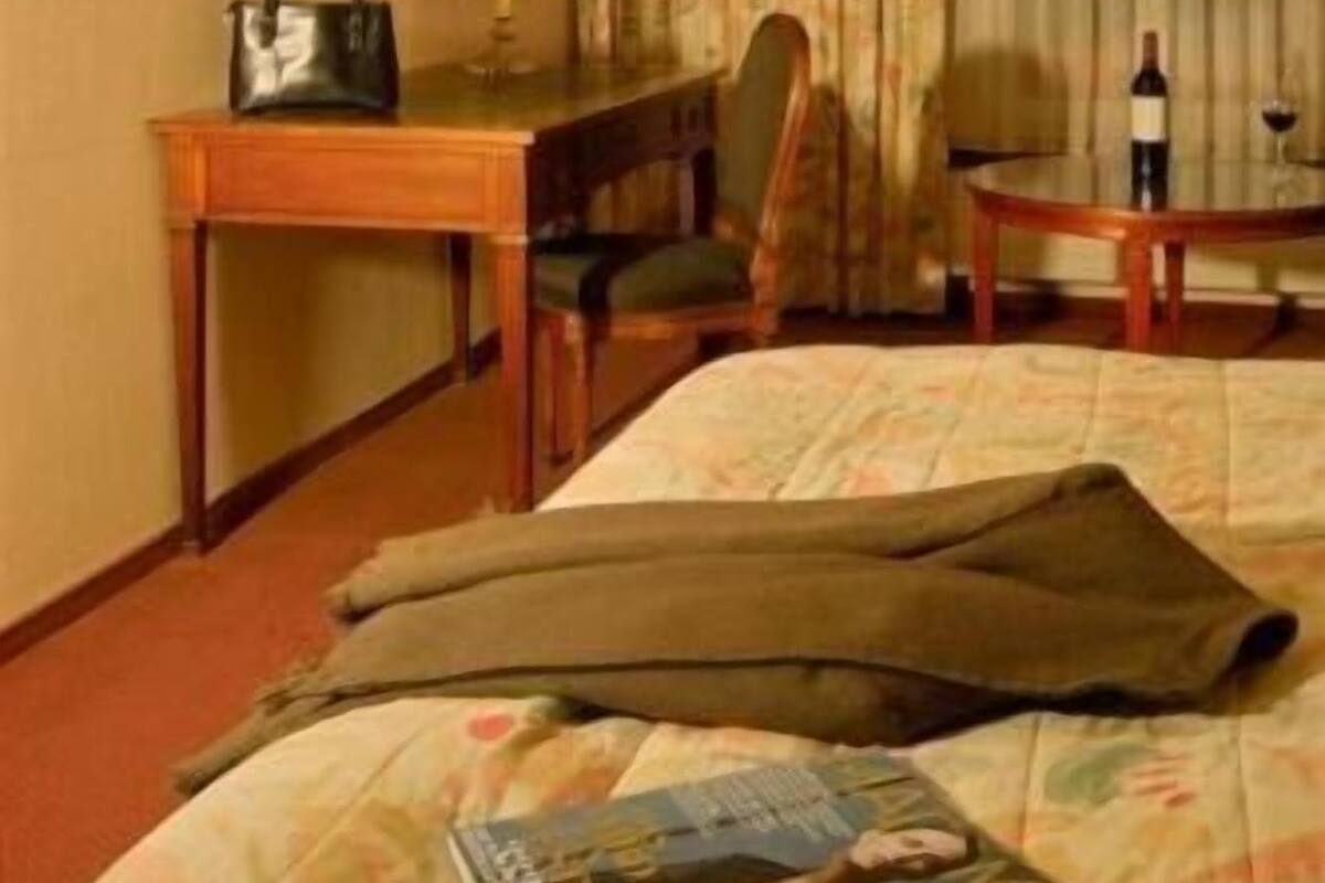 Habitación de hotel con cama, escritorio con lámpara, silla, televisor y ventana con cortinas.