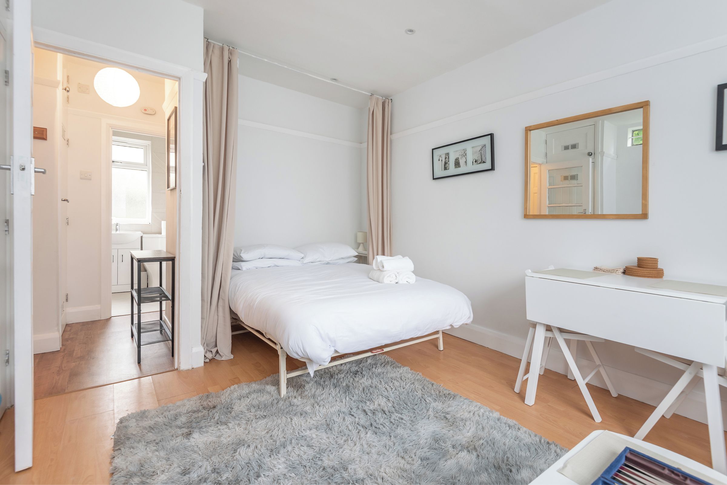 Quarto moderno com cama, mesa de cabeceira e escrivaninha com espelho.