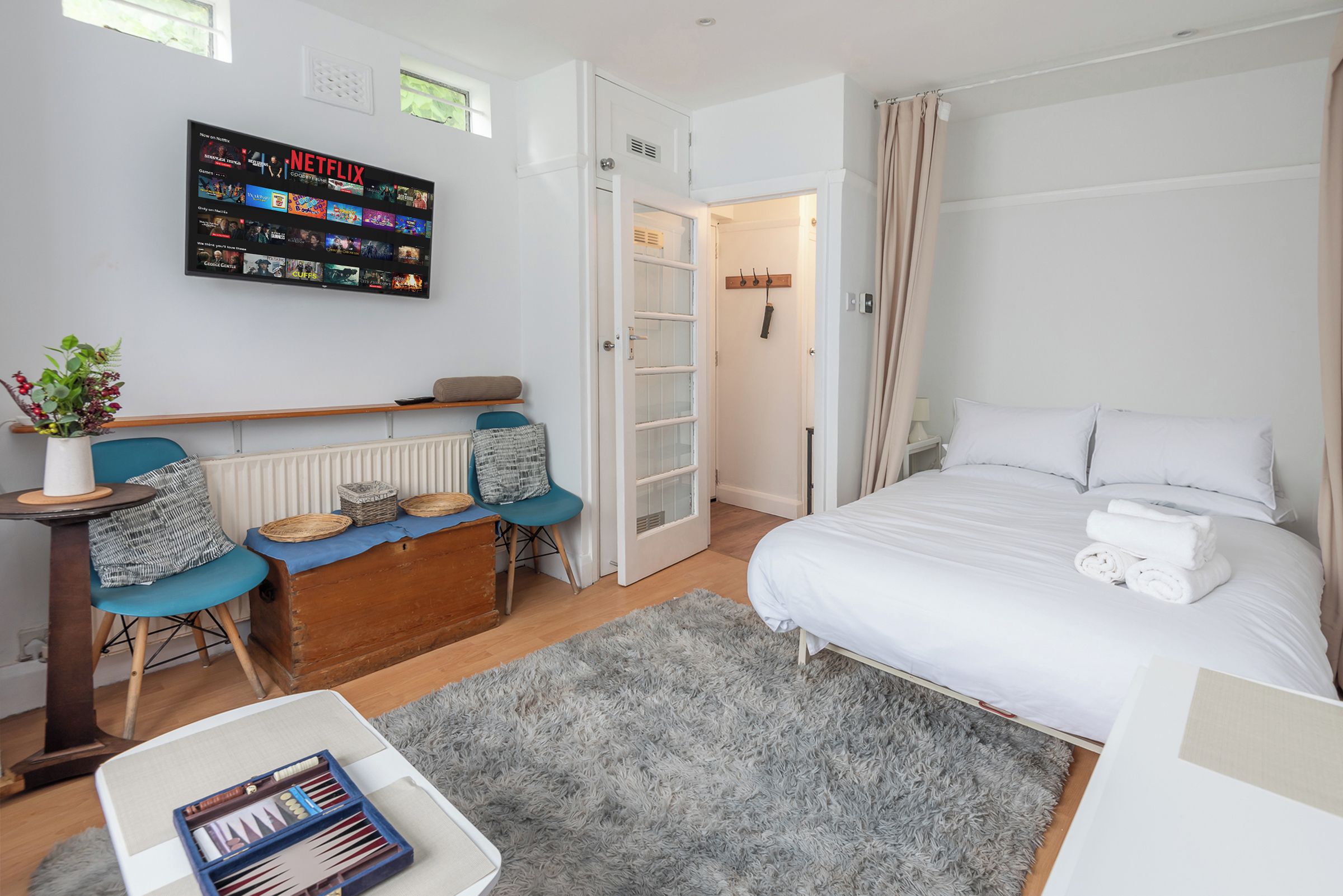 A modern bedroom with a bed, bedside table, chair, and a wall-mounted TV displaying a Netflix interface.