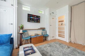 A living room with a blue sofa, a coffee table with books, a grey rug, a wall-mounted TV, and a wooden chest of drawers. - Bright Studio w Sun Trap Garden Wandsworth SW18 (Greater London)