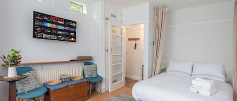 A modern bedroom with a bed, bedside table, chair, and a wall-mounted TV displaying a Netflix interface.