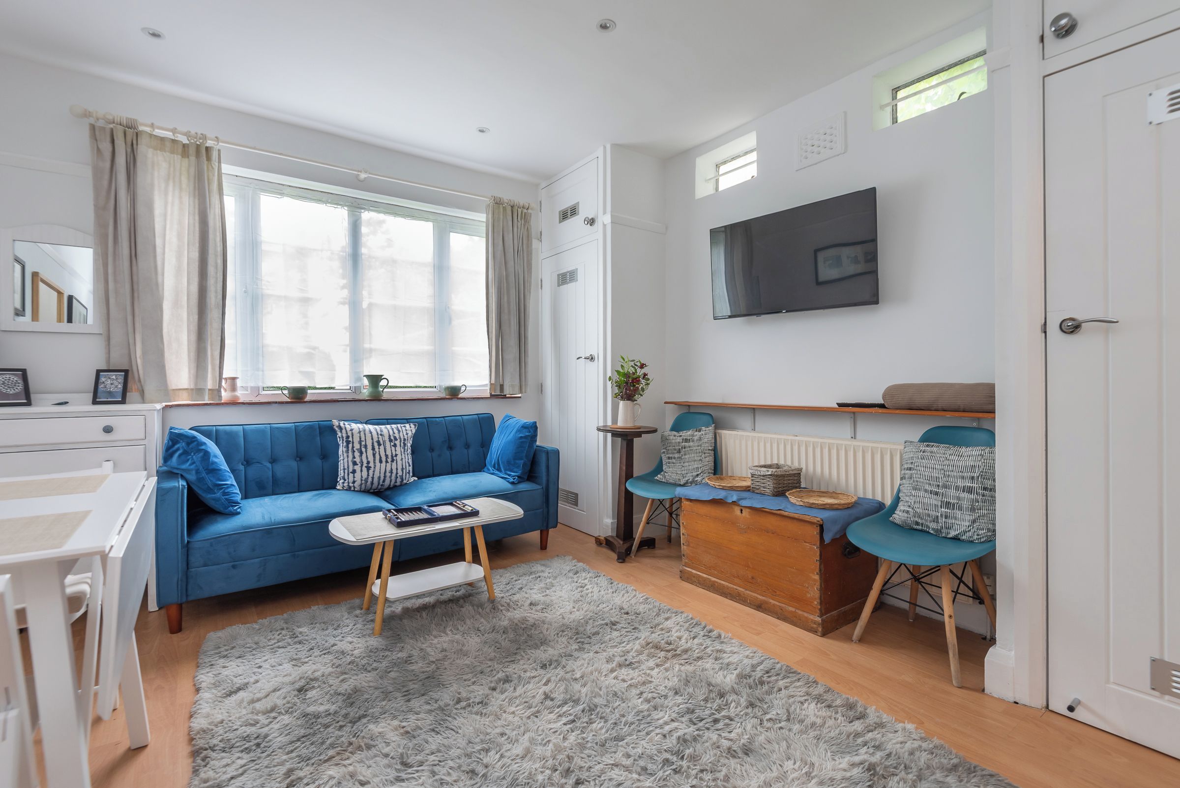 A modern living room with a blue sofa, a small table, a grey rug, and a TV mounted on the wall.