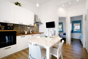 A modern kitchen with white cabinets, a microwave, and a stove. There's a dining table with chairs and a decorative boat on it.