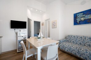 A modern living room with a flat-screen TV, a dining table with chairs, a sofa, and a painting on the wall.