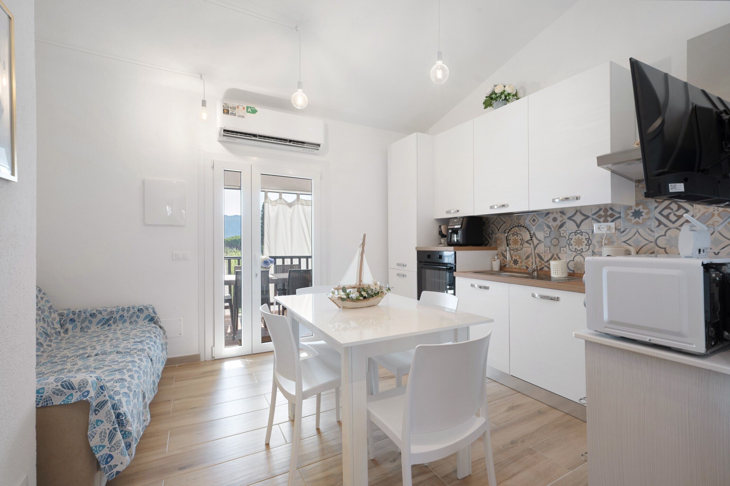 A compact kitchen with white cabinets, a dining table with chairs, a microwave, and a small decorative sailboat on the table.