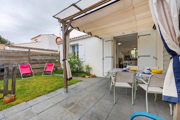 Eine Terrasse mit Tisch und Stühlen, ein Holzzaun und ein überdachter Bereich.
