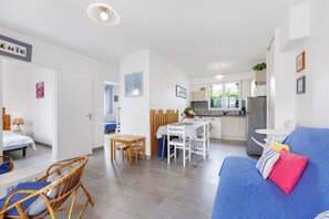 A modern, well-lit room with a dining table, chairs, a sofa, and a kitchen area. - Holiday Home 'Gîte « le Bel Air »' with Private Terrace, Private Garden and Wi-Fi (Saint-Gilles-Croix-de-Vie)