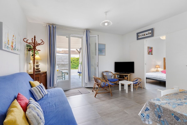 A room with a sofa, a TV, a bed, a dining table, and a chair. - Holiday Home 'Gîte « le Bel Air »' with Private Terrace, Private Garden and Wi-Fi (Saint-Gilles-Croix-de-Vie)