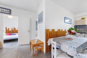 Ein Zimmer mit einem Bett, einem Holztisch, einem Esstisch mit floraler Dekoration und einer Küchenzeile.