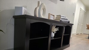 Um console de madeira escura com livros e uma pequena moldura na parede branca.