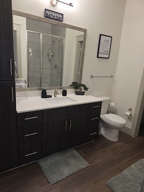 A bathroom with a dark wood vanity, a white sink, a large mirror, a potted plant, a toilet, and a sign above the mirror. - Cozy 1-bedroom apartment in charming Addison (Addison)