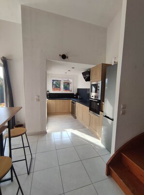 A modern kitchen with wooden cabinets, a black countertop, and a stainless steel refrigerator. - Villa Torreilles Plage 4 People (Torreilles)