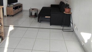 Ein modernes Wohnzimmer mit einem schwarzen Sofa, einer Holztrennwand, einem kleinen runden Tisch und einem Blumentopf.