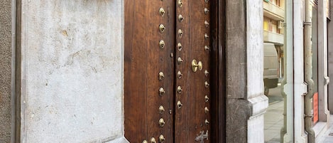 A hotel entrance with a large wooden door, a sign above it, and a stone wall.