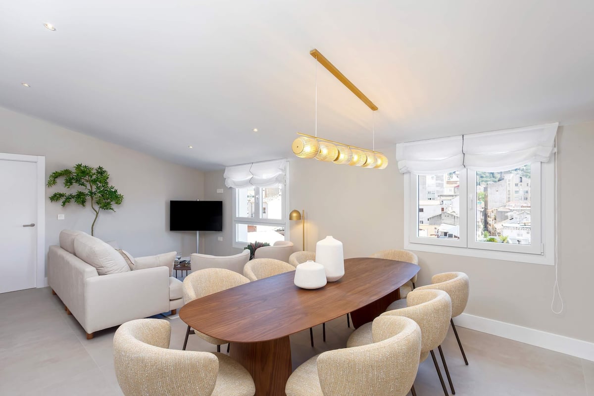Un salon moderne avec une table à manger en bois, des canapés de couleur beige et un téléviseur à écran plat.