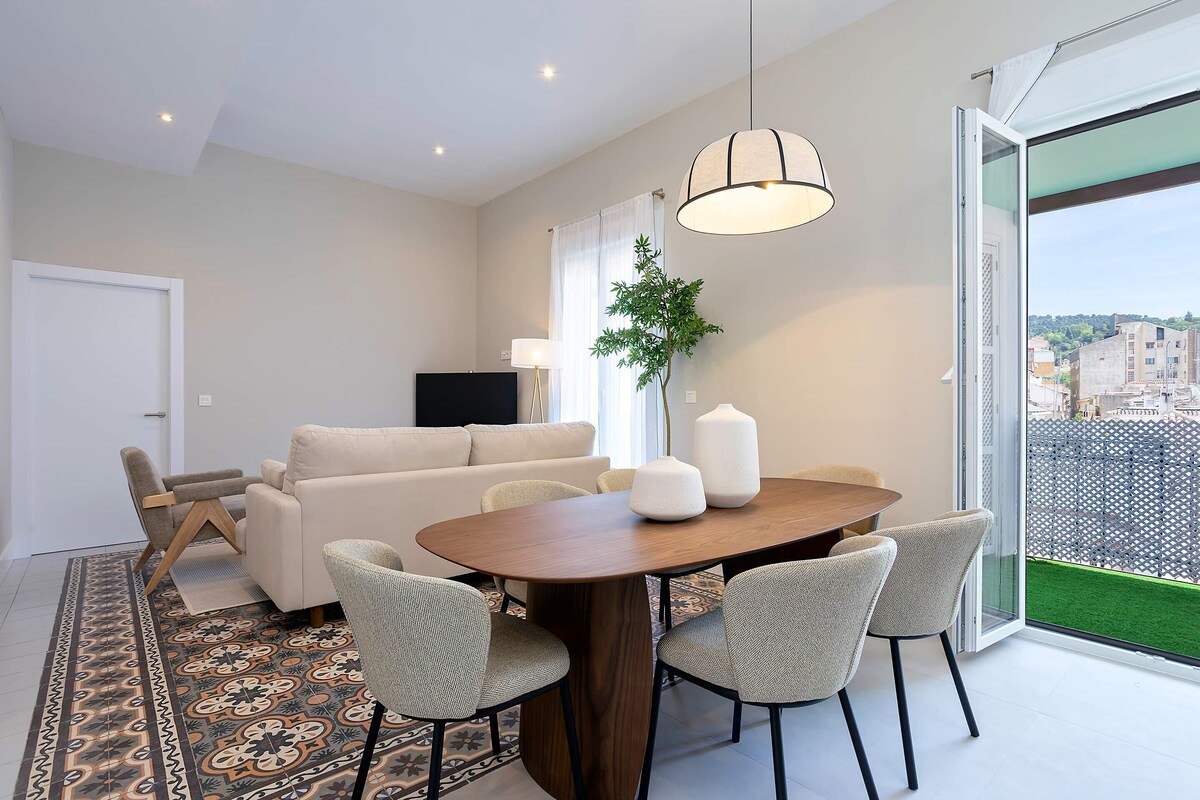 Una sala de estar moderna con comedor, sofá, televisor y un amplio ventanal con vistas.
