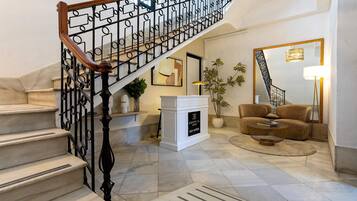 Una escalera con barandilla de hierro forjado que conduce a una plataforma, una chimenea blanca, un sofá y una mesa de centro en un salón.