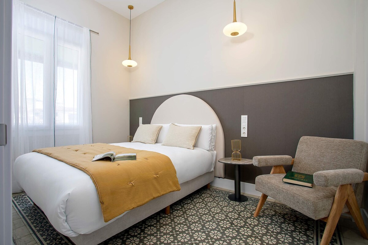 Una habitación de hotel con cama, una silla, una mesita y suelo estampado.