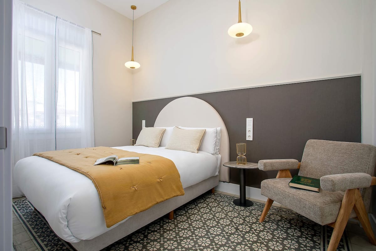 Une chambre d’hôtel avec un lit, une chaise, une petite table et un sol à motifs.