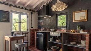 A compact kitchen with a checkered floor, a black refrigerator, and a wooden table with a stool. - CABRA - Casa do Burro (Setúbal)