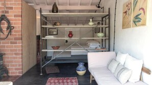 A room with a white sofa, a metal shelf unit with various items, a brick wall, and a painting. - CABRA - Casa do Burro (Setúbal)