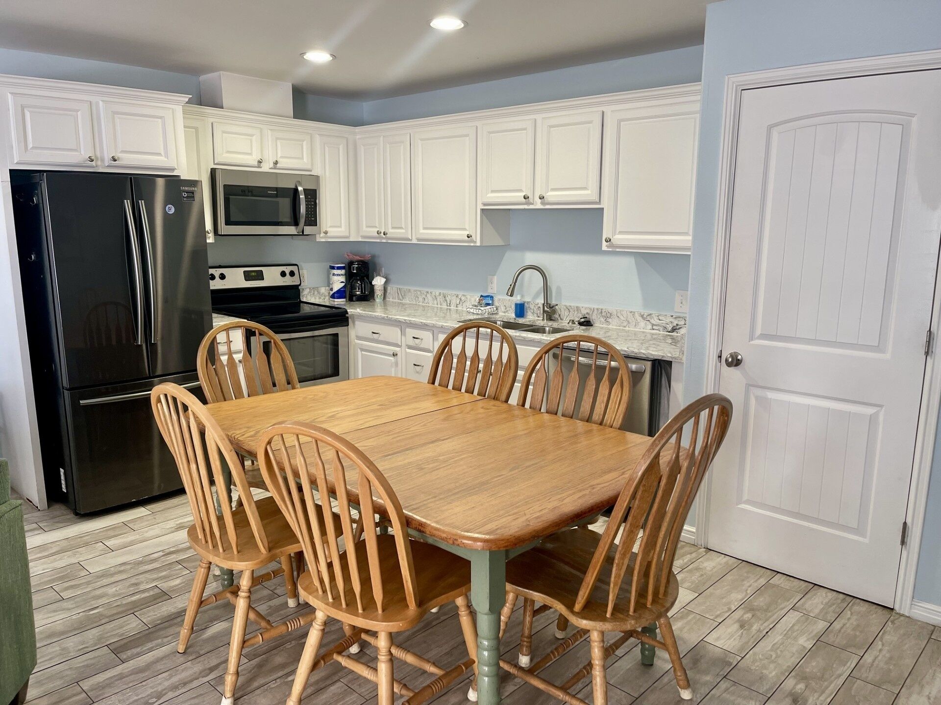A kitchen with white cabinets, a black refrigerator, a microwave, a stove, and a dining table with wooden chairs.