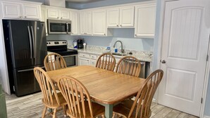 A kitchen with white cabinets, a black refrigerator, a microwave, a stove, and a dining table with wooden chairs. - Beachgate Condo Suites And Hotel 516 1 Bedroom Condo (Port Aransas)