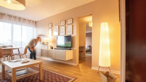 Ein modernes Wohnzimmer mit Fernseher, eine Essecke mit Tisch und Stühlen sowie ein Flur, der in einen weiteren Raum führt.
