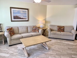 Ein Wohnzimmer mit zwei Sofas, einem Couchtisch, einer Lampe und einem gerahmten Bild an der Wand.