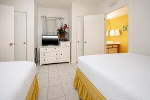 Ein Hotelzimmer mit zwei Betten, einem Fernseher, einem Schminktisch und einem durchgehenden Türbogen einsehbarer Badezimmer.
