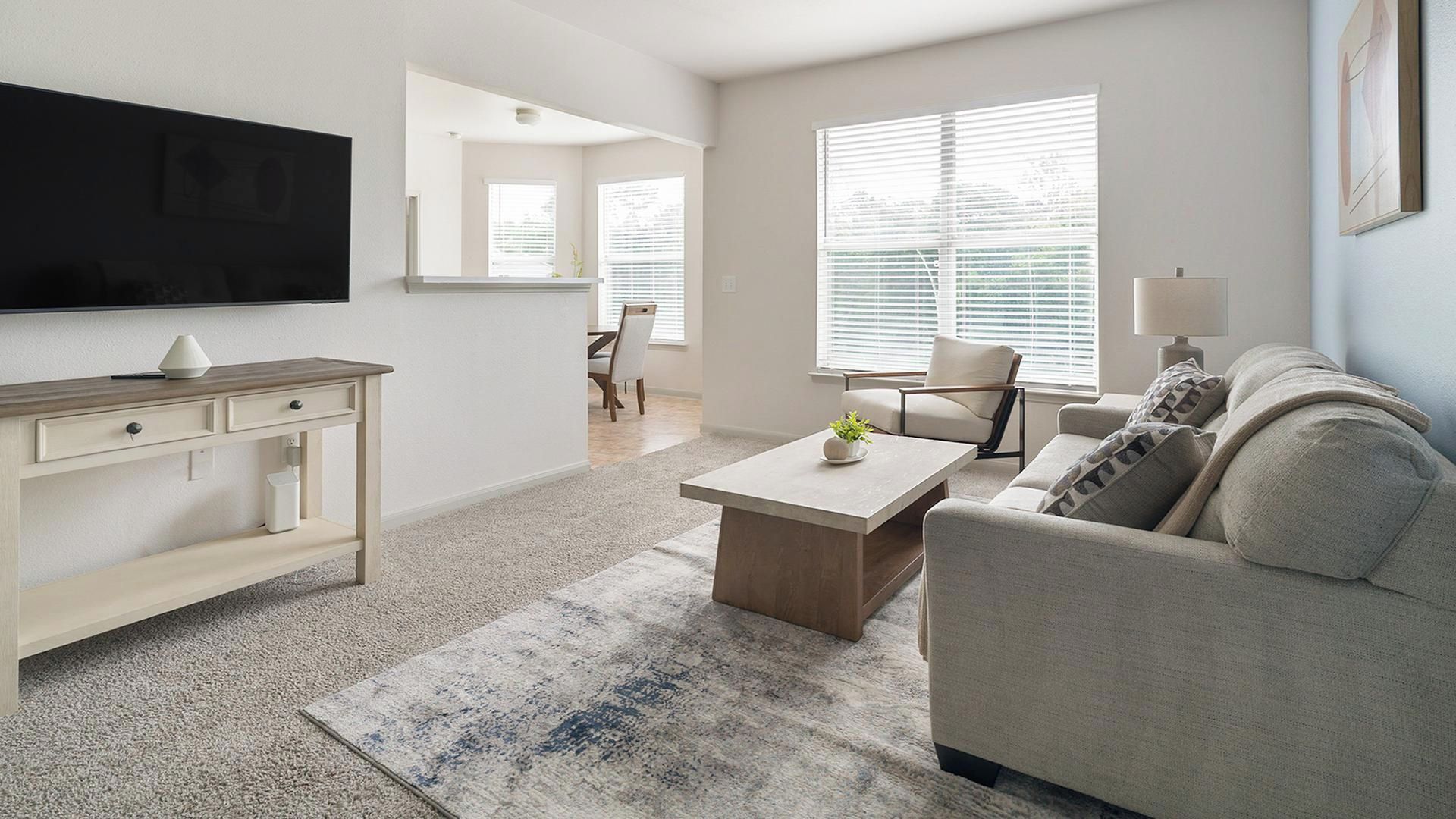Ein modernes Wohnzimmer mit Flachbildfernseher, Couchtisch, Sofa und einem Essbereich im Hintergrund.
