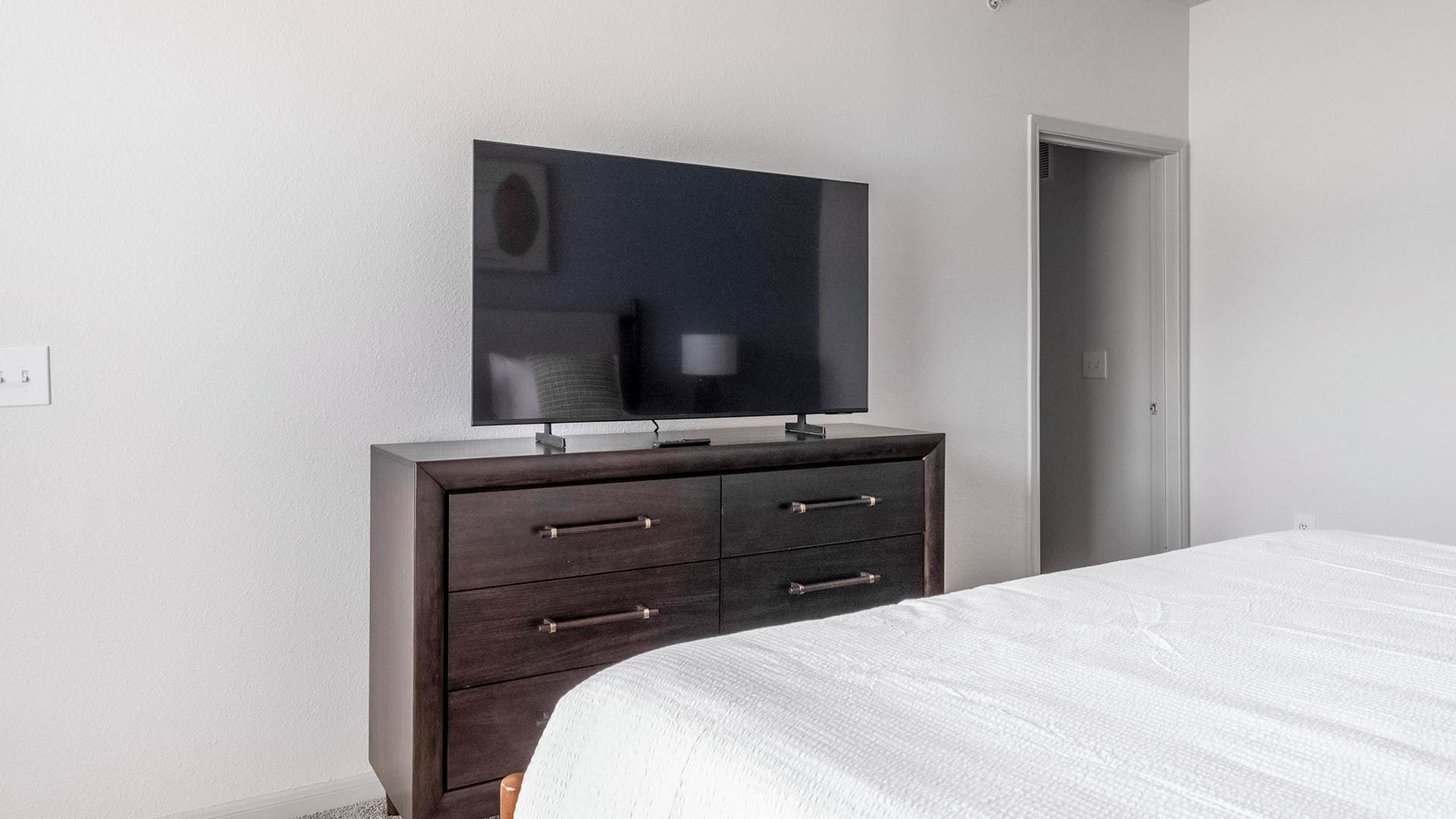 A bedroom with a bed, a dresser, a television, and a door.