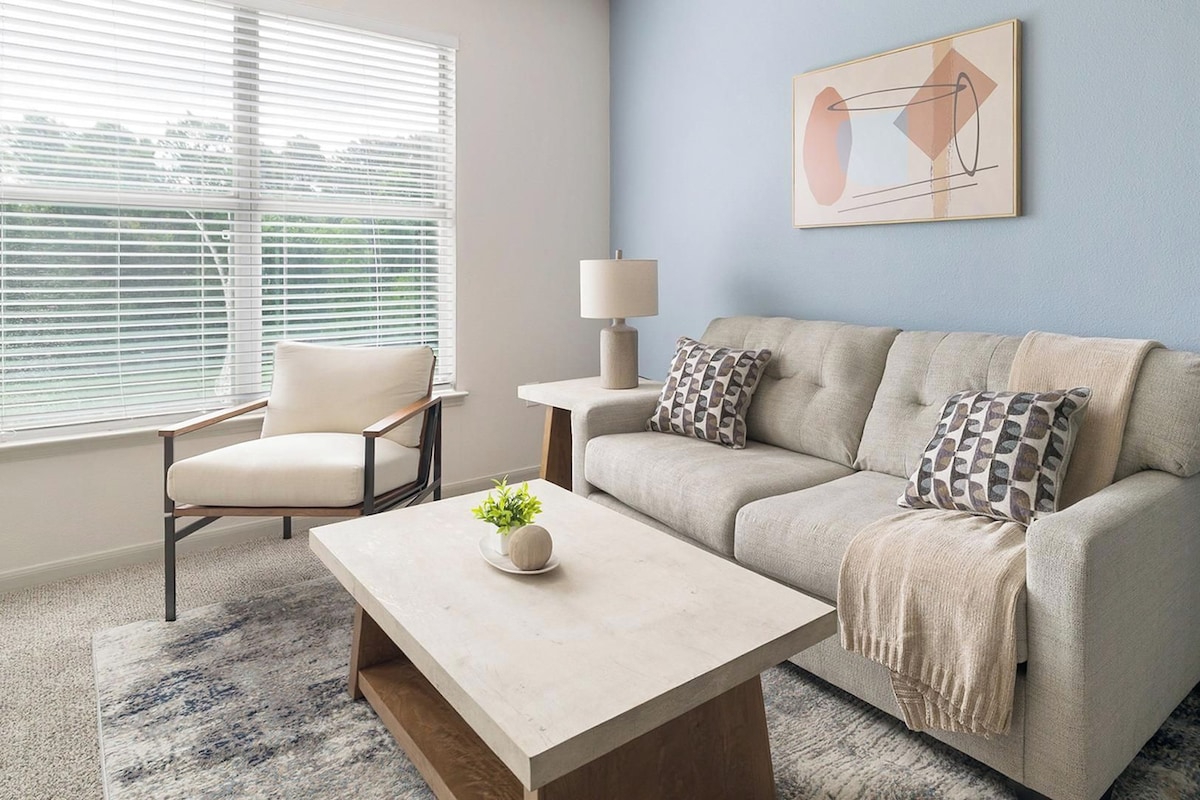 A living room with a sofa, armchair, coffee table, and a lamp.