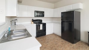 A kitchen with white cabinets, a black refrigerator, a microwave, a stove, and a sink.