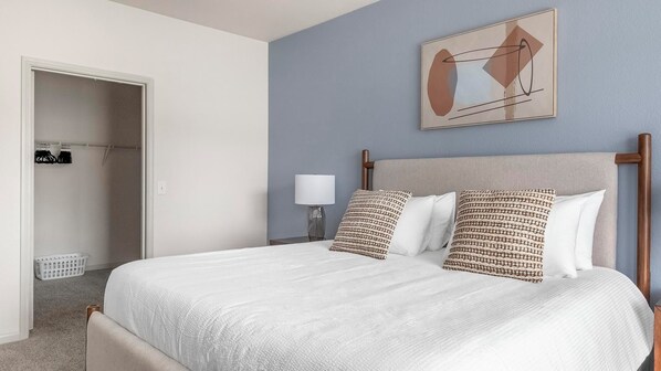 A hotel room with a bed, a nightstand, a lamp, a closet, and a wall art piece. - Landing Apartments Humble near Bordersville (Humble)