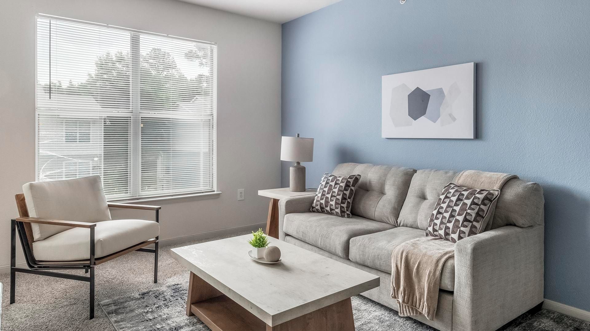 A living room with a sofa, armchair, coffee table, and a lamp.